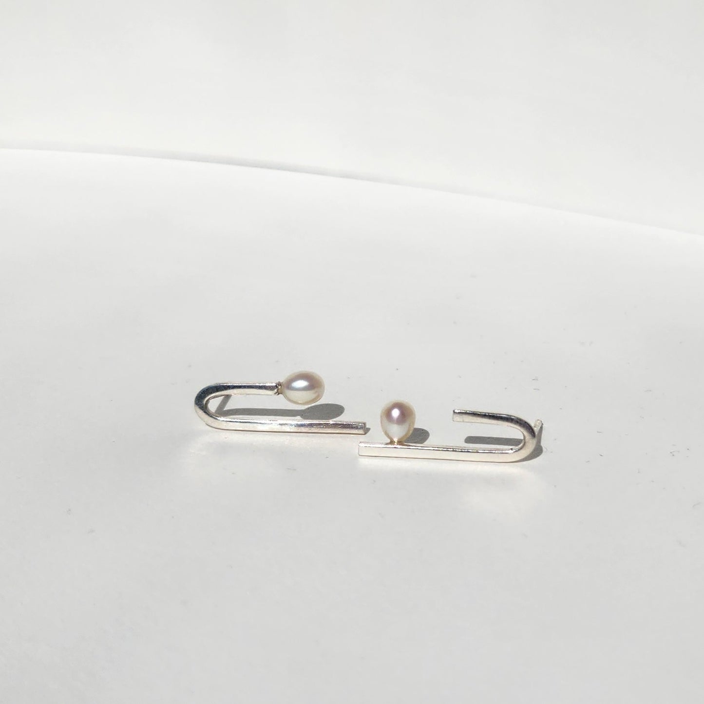 Close-up of Flexion Earrings: A detailed view of the handcrafted 925 sterling silver Flexion Earrings featuring oval freshwater pearls, highlighting their unique curved design.