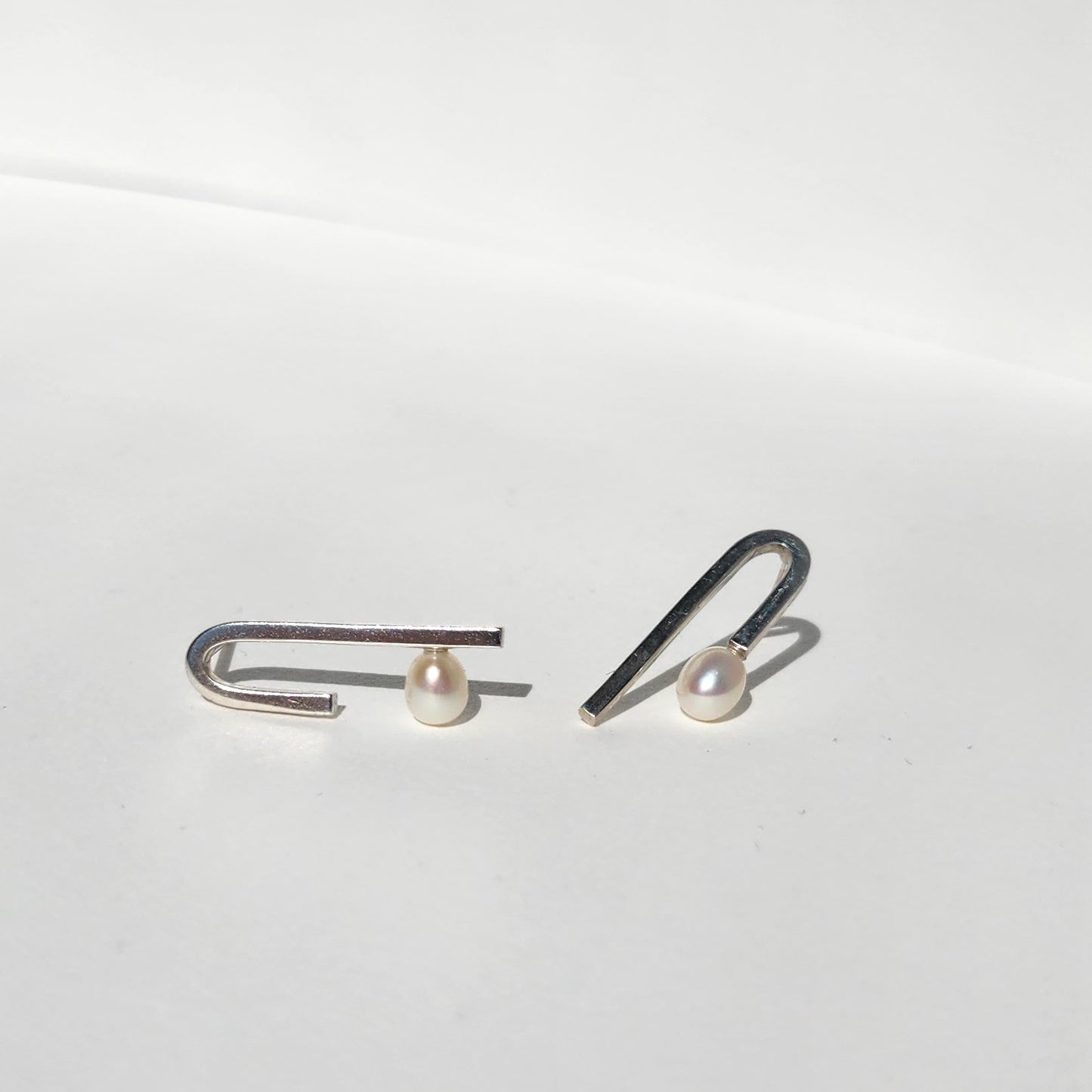 Close-up of Flexion Earrings: A detailed view of the handcrafted 925 sterling silver Flexion Earrings featuring oval freshwater pearls, highlighting their unique curved design.