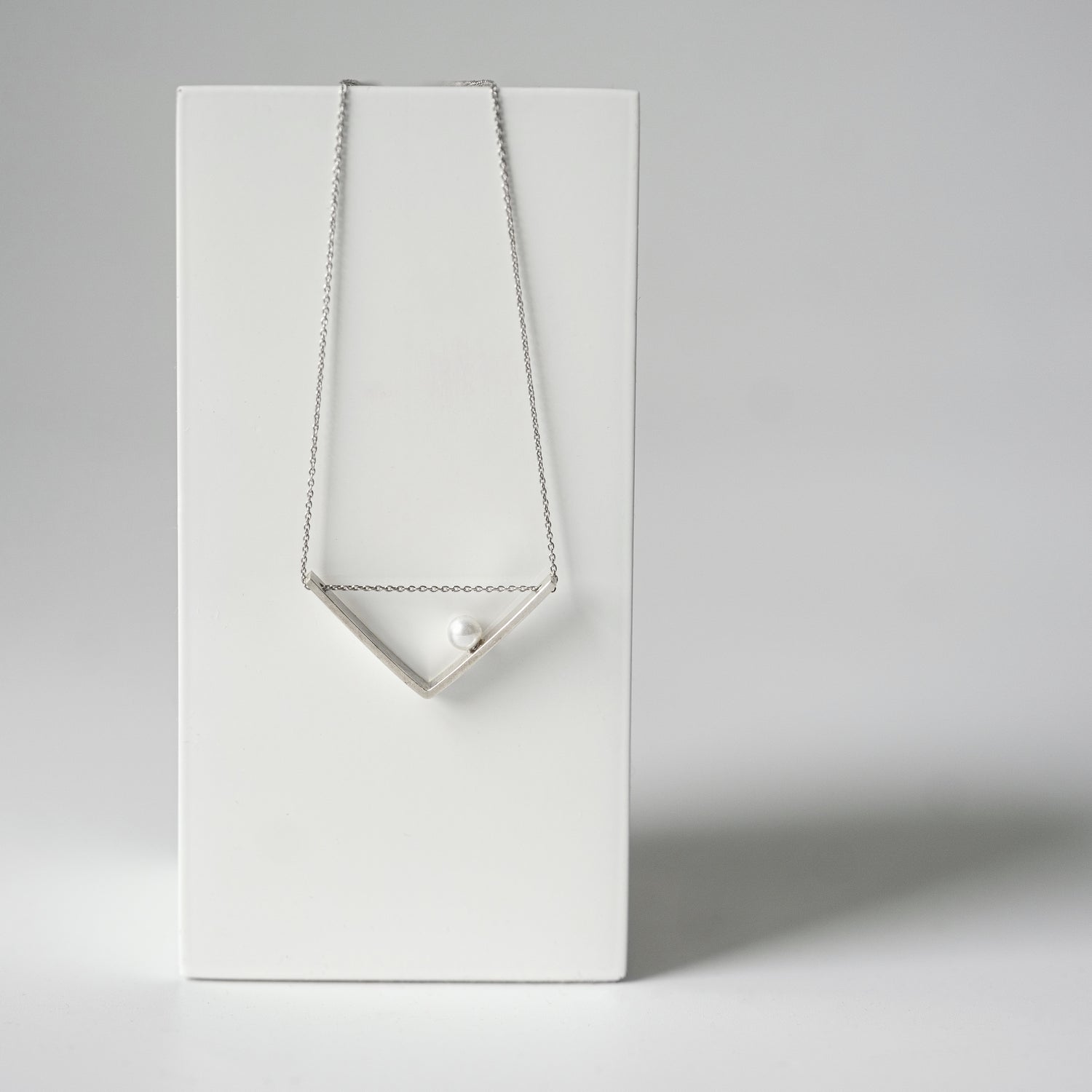 The necklace elegantly positioned on a display stand, capturing its sleek V-shaped design and the luminous glow of the freshwater pearl.